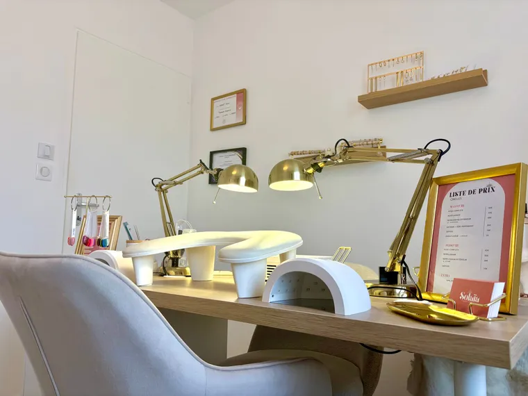 Poste de manucure de l’Institut Solaïa vu depuis le fauteuil de la cliente : lampes dorées, lampe UV et liste de prix encadrée